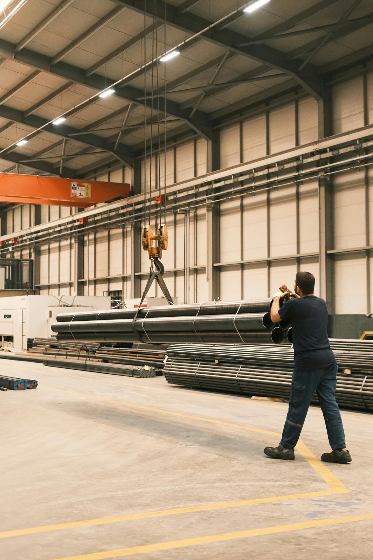 Overhead crane lifting industrial pipes in a warehouse